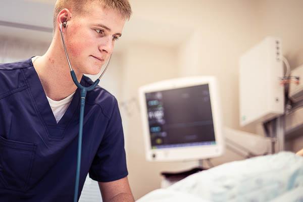 护理系学生Josh Zeitler在模拟病人身上使用听诊器